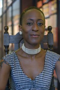 a woman stares into the camera. She is wearing a black and white shirt as well as a pearl choker and large pearl earrings